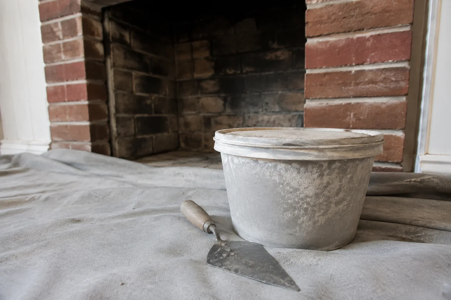 Closed container and trowel at a cold brick fireplace.